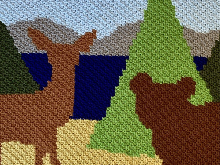 a blanket made with the mini-C2C stitch, featuring a deer and a bear looking at a lake
