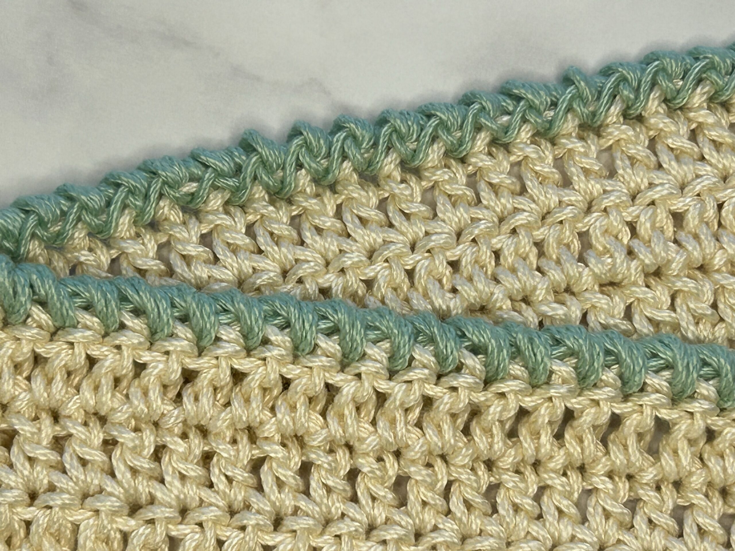 An off-white crochet piece with a green forward crab stitch border