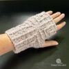 A left hand in a crocheted fingerless glove. The mitt has a cable pattern at right angles from the center of the back of the hand.