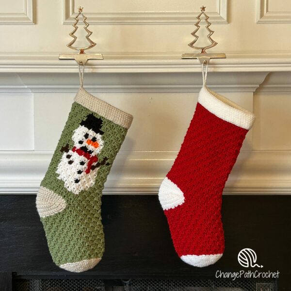 2 Christmas stockings hanging from a mantle. One is solid red, and the other is green with the image of a snowman on it.