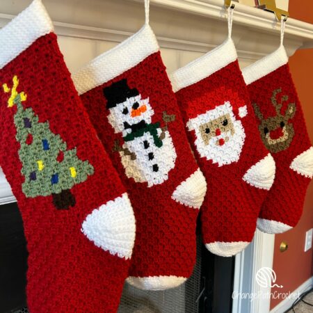 Four crochet Christmas stockings lined up hanging on a mantle. Each has a different image crocheted on the front: tree, snowman, santa, and reindeer.