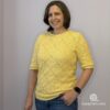 Woman standing with one hand in her pocket, wearing a yellow, handmade Tunisian crochet shirt with half sleeves.